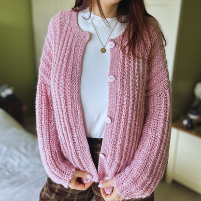 Person wearing a pink knitted cardigan with buttons indoors.